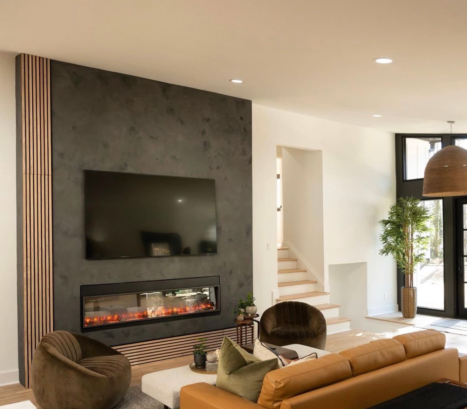 Dark charcoal microcement fireplace wall with a wood slat accent in a modern living room